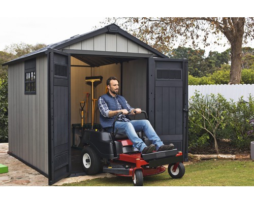 Un homme conduit un tracteur de jardin dans un abri de jardin pour l''entretien de la pelouse.