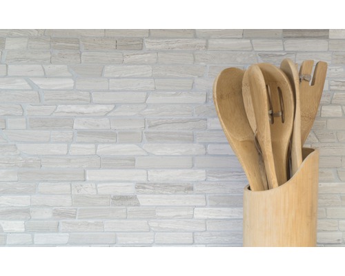 Küchenutensilien aus Holz in einem Halter vor einer Steinwand