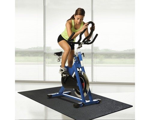 Frau trainiert auf einem blauen Indoor-Cycling-Bike auf einer schwarzen Matte