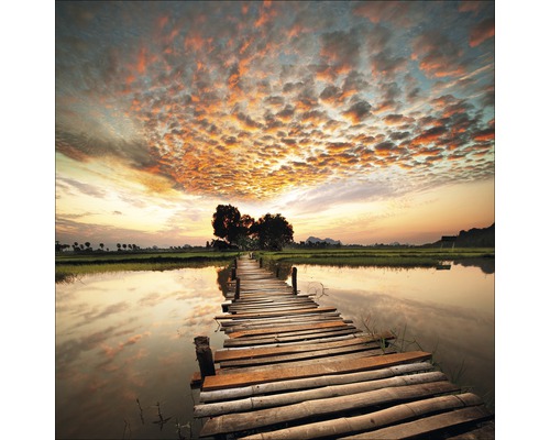 Passerelle en bois au-dessus d''un plan d''eau avec des champs et des arbres sous un ciel nuageux.