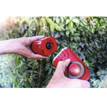 Zwei Hände halten eine elektronische Marderscheuche vor grünem Laub