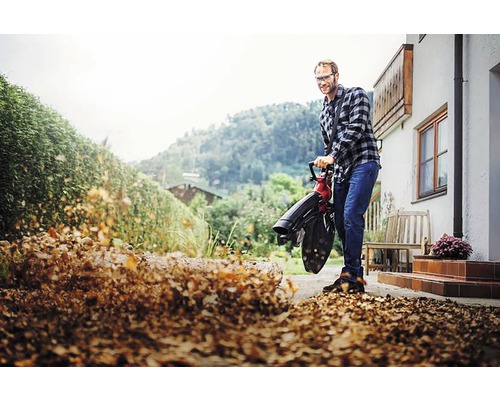 Ein Mann benutzt einen Laubbläser, um Laub zu entfernen.