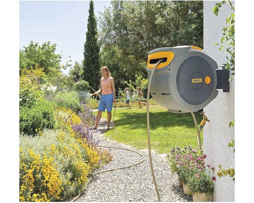Une femme arrose des plantes avec un dévidoir dans le jardin.