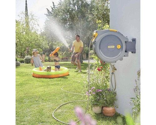 Scène de jardin avec boîte à tuyau au mur, famille jouant dans la piscine avec un jet d''eau