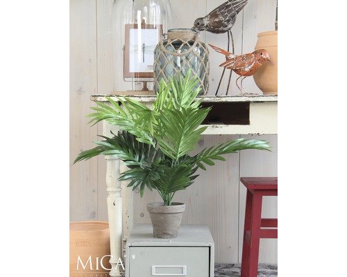 Dekorative Kunstpflanze im Topf auf einem Beistelltisch, umgeben von weiteren Dekorationselementen.