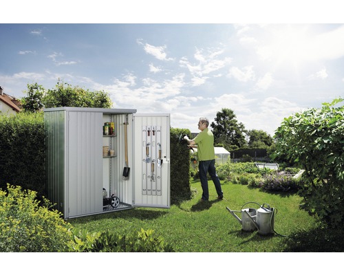 Gartenszene mit Metallgerätehaus, Gartengeräten und Gärtner beim Heckenschneiden