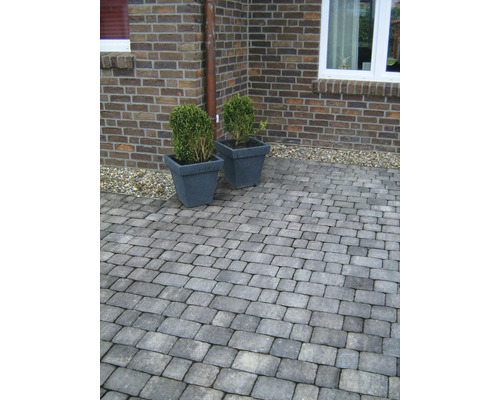 Aussenbereich mit Pflastersteinen und zwei Pflanzenkübeln vor einer Backsteinmauer.