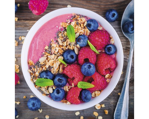 Bol avec smoothie, myrtilles, framboises et muesli sur une table en bois
