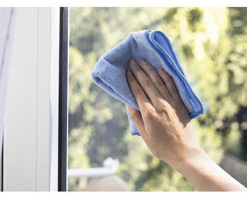 Eine Hand reinigt ein Fenster mit einem Mikrofasertuch.