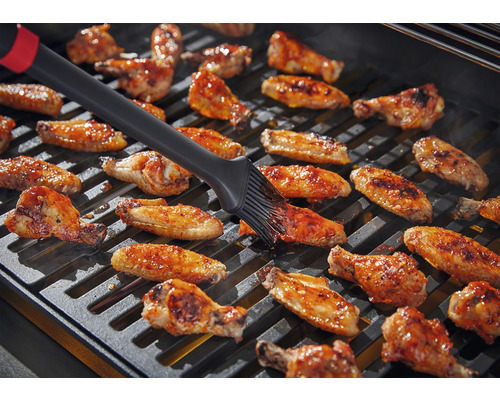 Des ailes de poulet sont badigeonnées sur un gril avec une brosse.