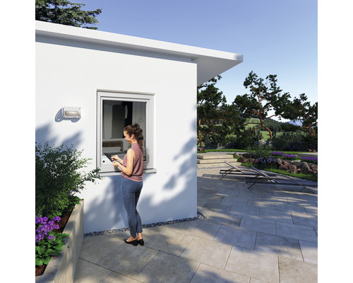 Femme avec tablette devant une maison avec fenêtre et jardin