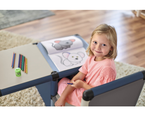 Mädchen sitzt an einem Kindertisch mit Stiften und Malbuch