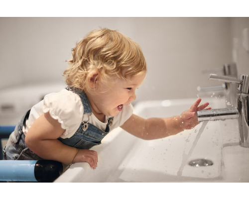 Kind spielt mit Wasser am Waschbecken mit Wasserhahn