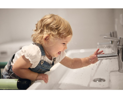 Kind spielt mit Wasserhahn im Badezimmer Waschbecken