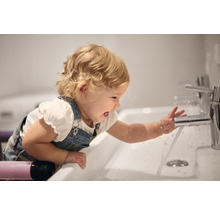 Un enfant joue avec un robinet dans une salle de bains.