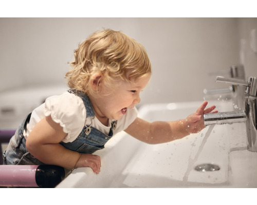 Ein Kind spielt mit einem Wasserhahn in einem Badezimmerwaschbecken.