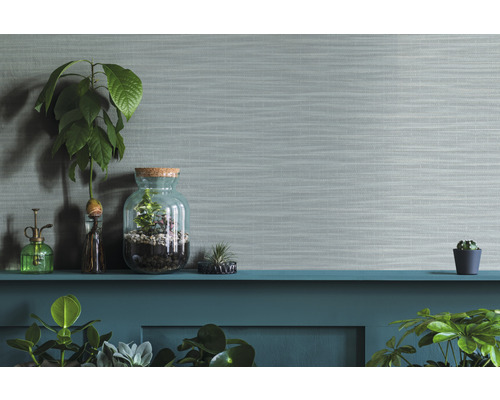 Dekorative Zimmerpflanzen in Gläsern und Töpfen auf einem Regal vor einer strukturierten Wand.