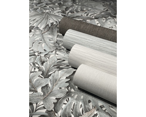 Drei Tapetenrollen liegen auf einer Tapete mit Pflanzenmuster.