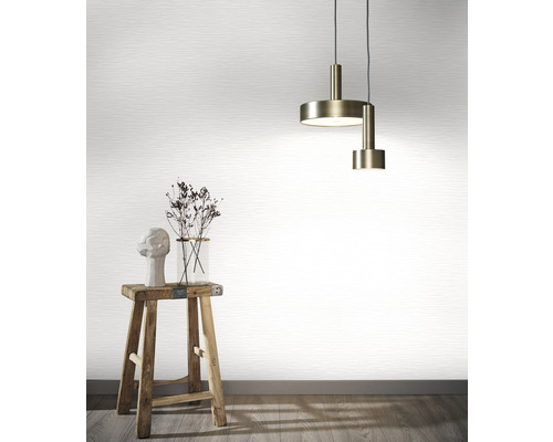 Szene mit einer Pendelleuchte, einer Vase mit Blumen, einer Skulptur auf einem Hocker vor einer Tapete.