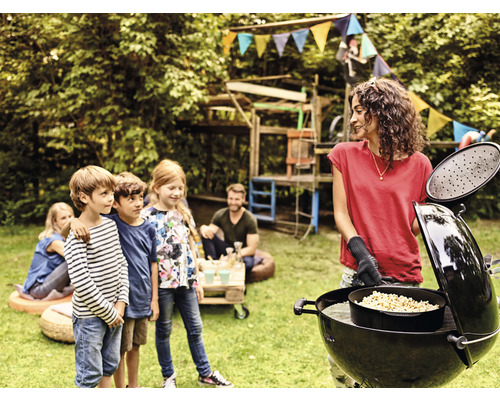 Une femme fait un barbecue dans le jardin avec des enfants et un barbecue sphérique.
