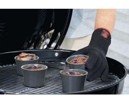 Une personne portant un gant de barbecue place des ramequins contenant des gâteaux aux myrtilles sur un gril.