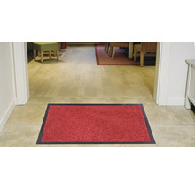 Tapis de sol rouge avec bord foncé devant une entrée de maison.