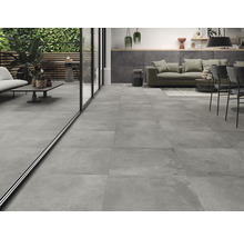 Intérieur avec carrelage gris, mobilier de salon et vue sur une terrasse avec plantes