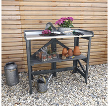 Gartentisch mit Pflanzen, Töpfen und Gartengeräten auf Kies