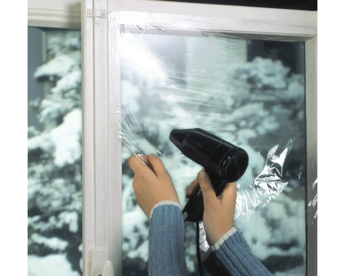 Une personne fixe un film de fenêtre avec un sèche-cheveux sur une fenêtre pour l''isolation thermique.