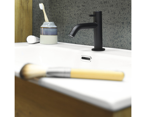 Schwarzer Waschtischmischer auf einem weißen Waschbecken mit Zahnbürste, Zahncreme und Make-up Pinsel