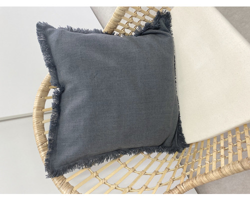 Coussin décoratif en tissu avec des franges sur un fauteuil en rotin