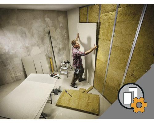 Mann montiert Gipskartonplatten an einer Wand mit Dämmmaterial und Metallprofilen