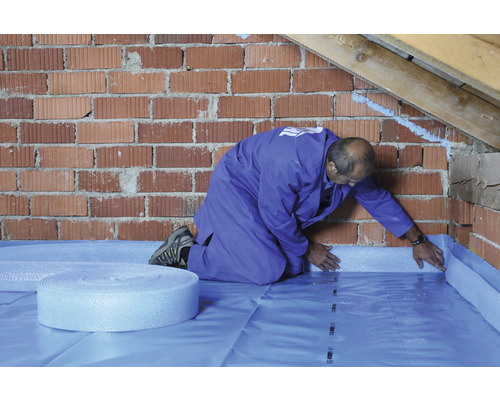 Handwerker verlegt Dämmunterlage auf einem Dachboden mit Ziegelwänden