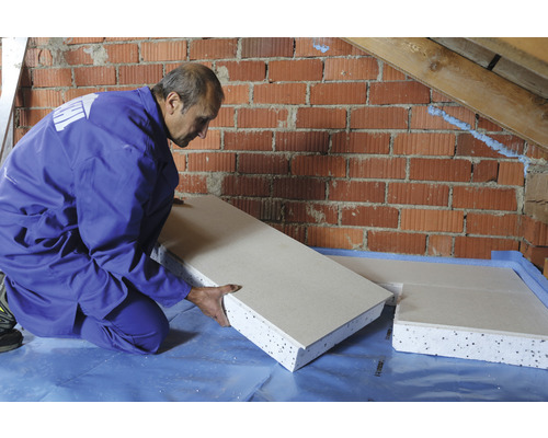 Ein Mann kniet und verlegt eine Dämmplatte an einer Ziegelwand.