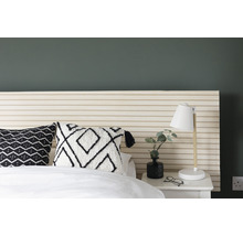 Schlafzimmerszene mit Bett, Nachttisch, Lampe und dekorativen Kissen.