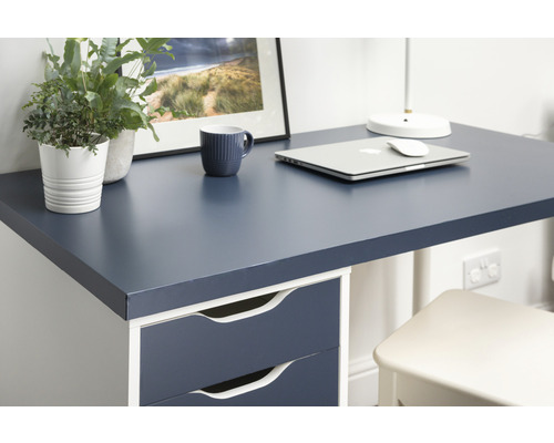 Detailansicht eines Schreibtisches mit dunkelblauer Platte, Schubladen, Laptop, Tasse und Dekoration