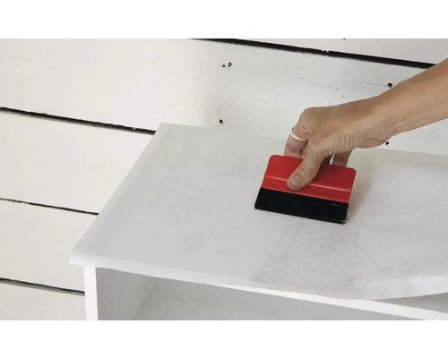 Application de film pour meubles avec une raclette sur un meuble.