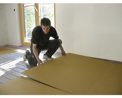 Mann verlegt Dämmplatten auf einer Fußbodenheizung im Innenraum