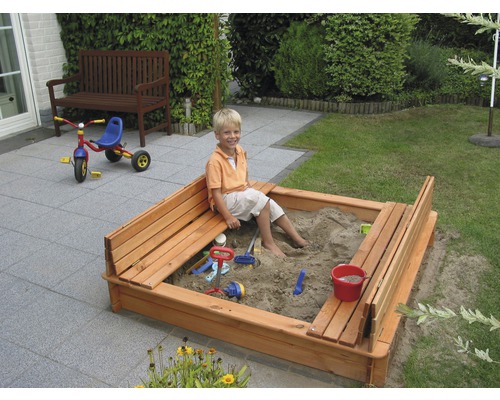 Sandkasten aus Holz mit Jungen und Spielzeug im Garten.