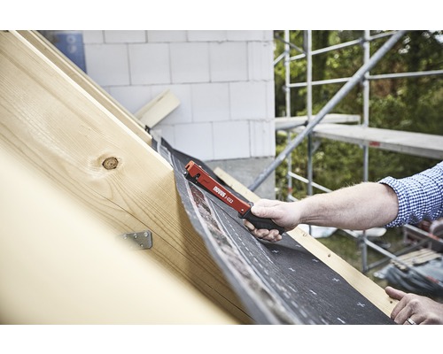 Handwerker befestigt Dachfolie mit einem roten Novus J-022 Klammergerät auf einem Dachstuhl.