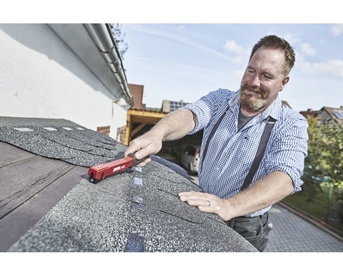 Handwerker befestigt Bitumenschindeln mit einem Dachpappnagler auf einem Dach.