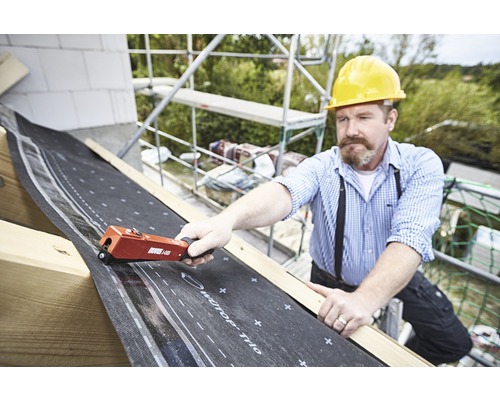 Ein Handwerker befestigt eine Dachbahn mit einem Handtacker auf einem Dach.