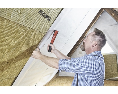 Ein Mann befestigt Dämmwolle mit einer Dampfbremsfolie an einer Dachschräge.