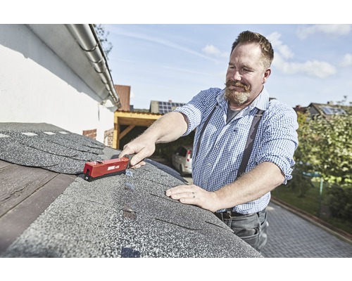 Ein Mann befestigt Bitumenschindeln mit einem Dachpappnagler auf einem Dach.