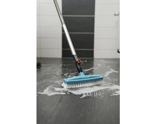 Brosse avec manche nettoie un sol carrelé