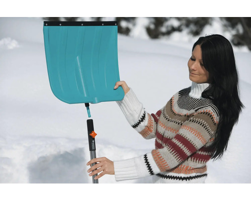 Une femme assemble une pelle à neige devant un fond enneigé
