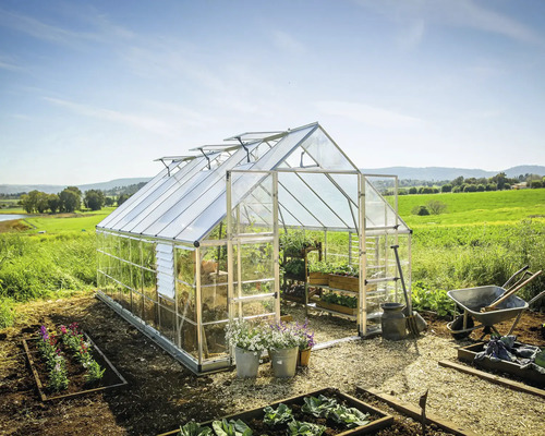Gewächshaus Palram – Canopia Balance Polycarbonat 0,7 mm 304 x 484 cm silber Gewächshaus mit Pflanzen, Schubkarre und Gartengeräten in einem Garten