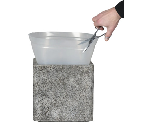 Eine Person schneidet mit einer Schere einen Kunststoffeinsatz auf einem Pflanzgefäß zu.