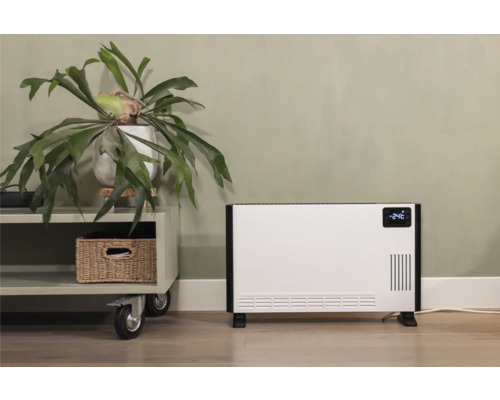 Weißer Konvektionsheizer neben einem Beistelltisch mit einer Zimmerpflanze und einem Korb