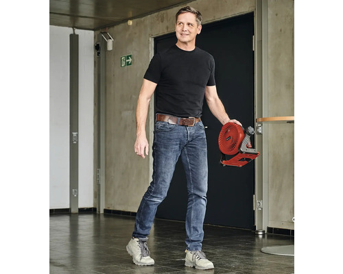 Un homme transporte un ventilateur sans fil dans un couloir